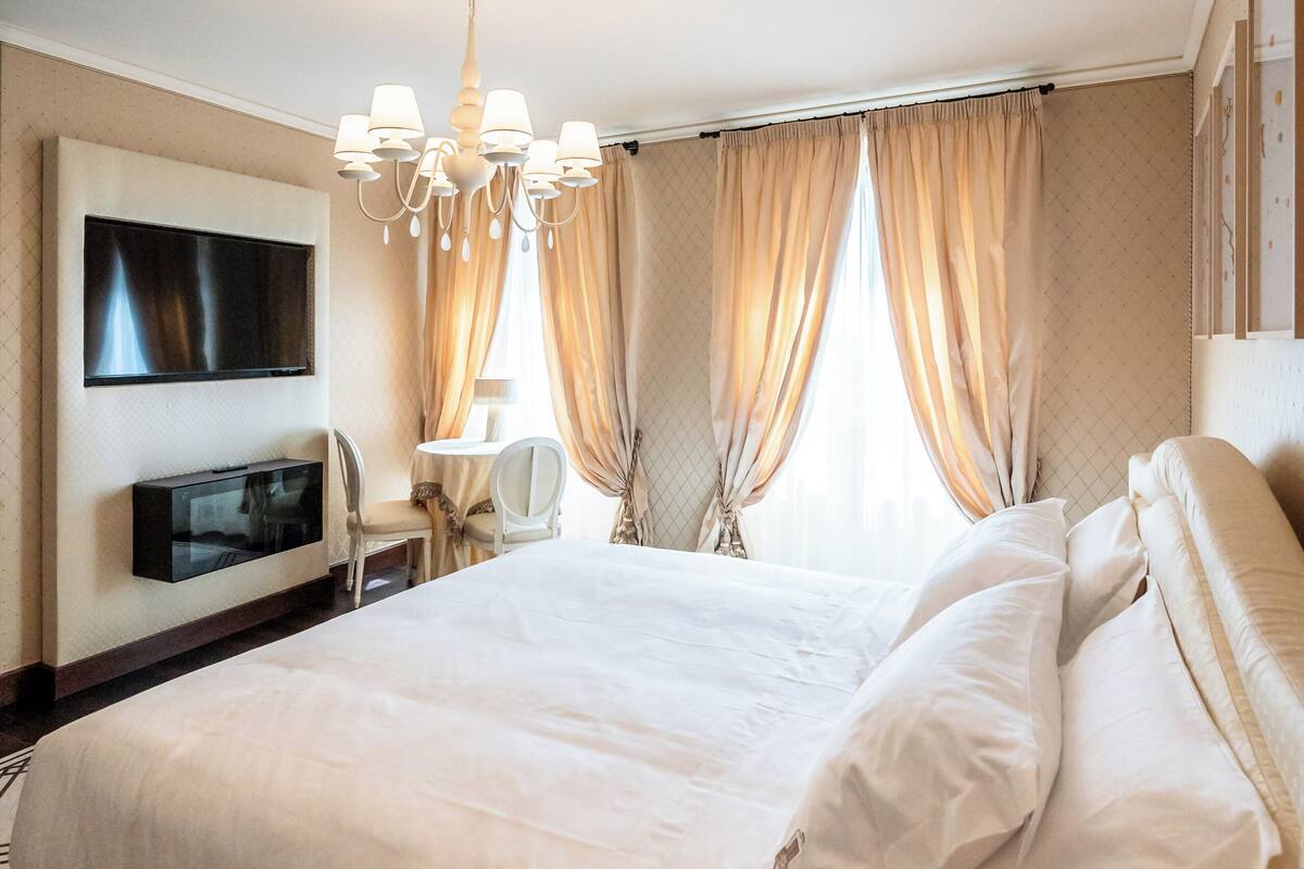 Une chambre d’hôtel avec un grand lit, un téléviseur fixé au mur, un bureau avec une chaise et un lustre.