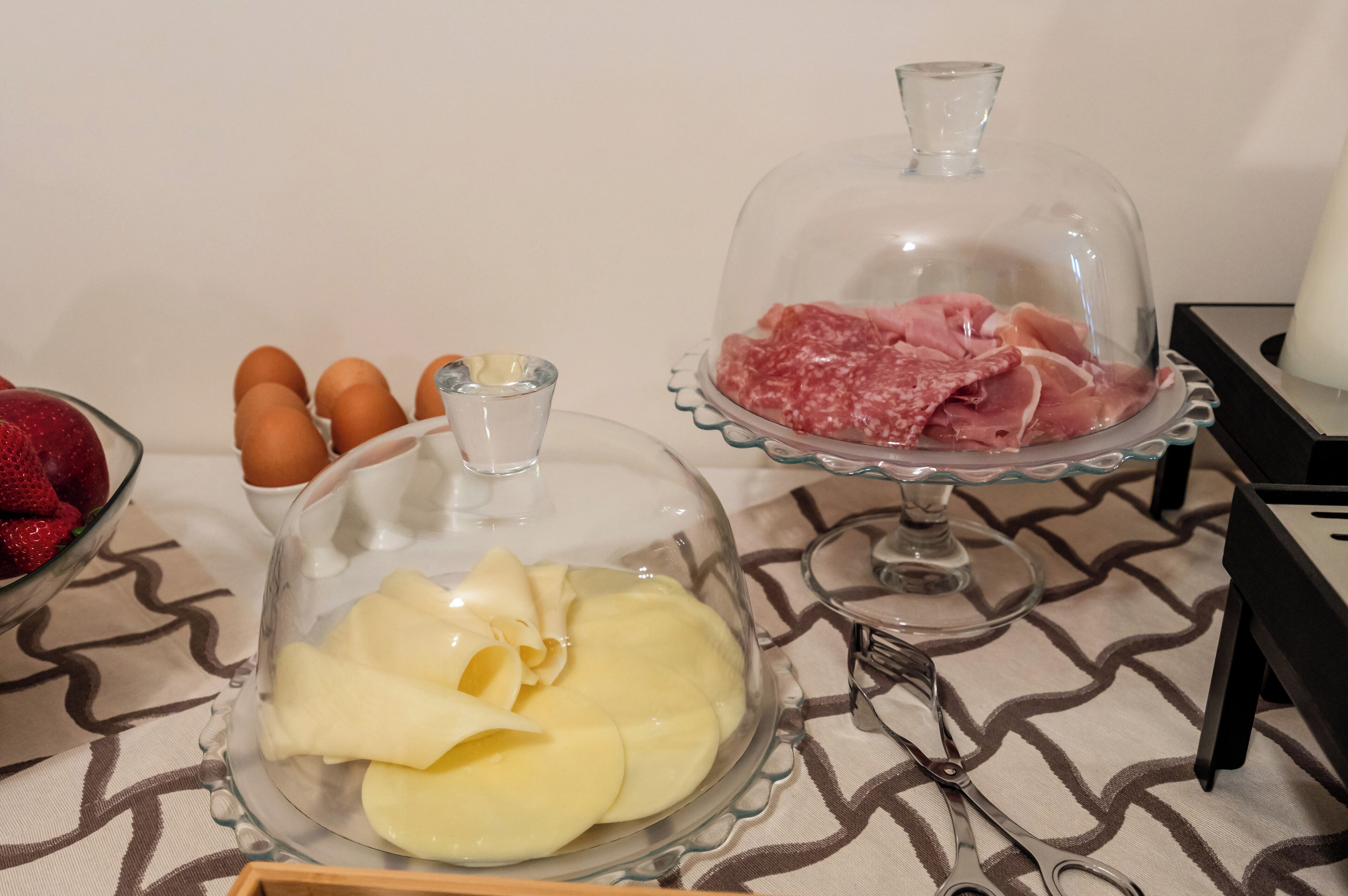 A table with a glass bowl containing sliced apples and a glass dome covering a dish of sliced meat.