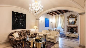 Ein großzügiges Wohnzimmer mit einer Chandelüster, Sofas, einem Kamin und einem großen Gemälde an der Wand.
