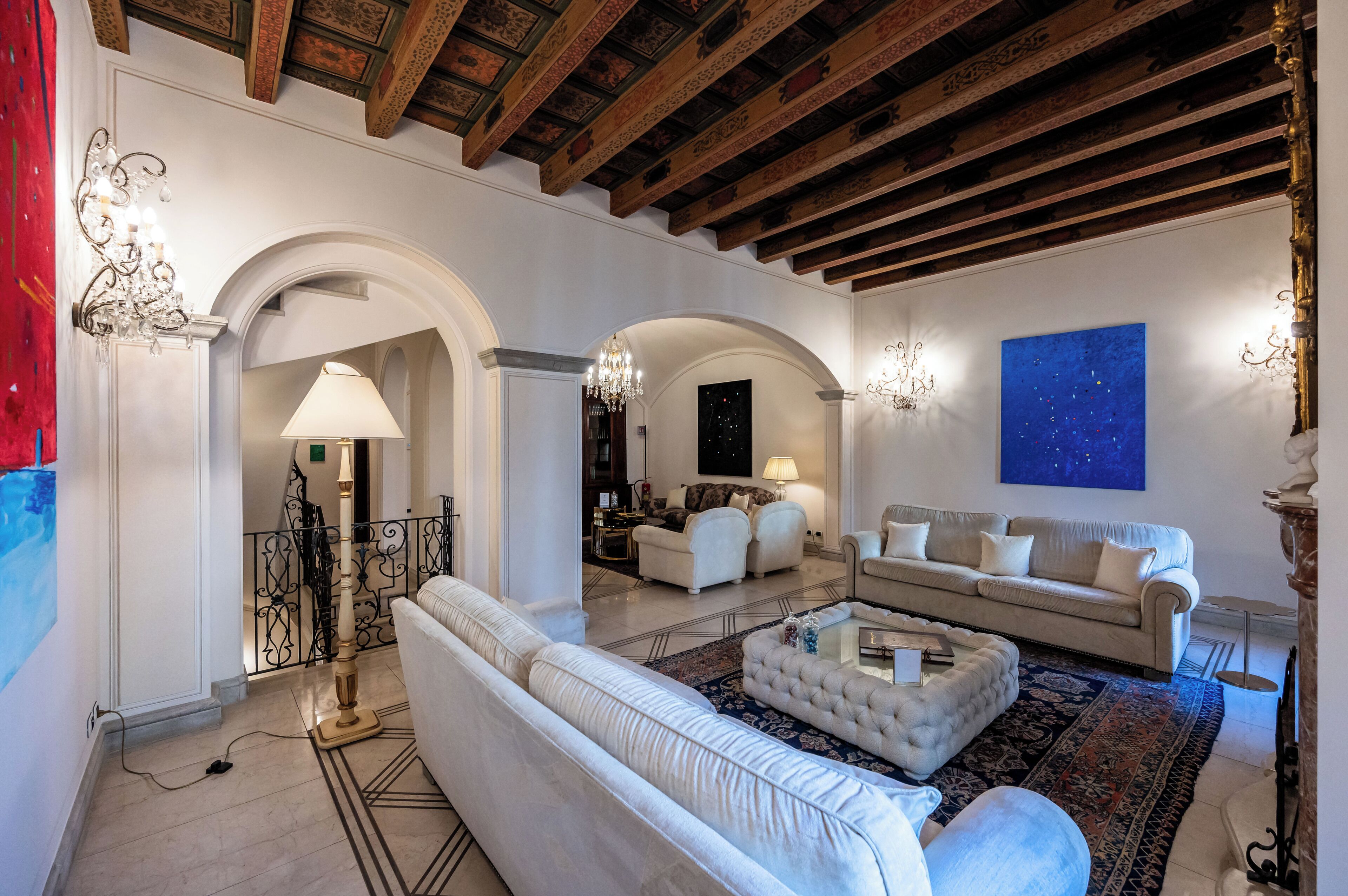 A spacious living room with a high ceiling, white sofas, a coffee table, and a large painting on the wall.