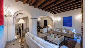 A spacious living room with a high ceiling, white sofas, a coffee table, and a large painting on the wall.