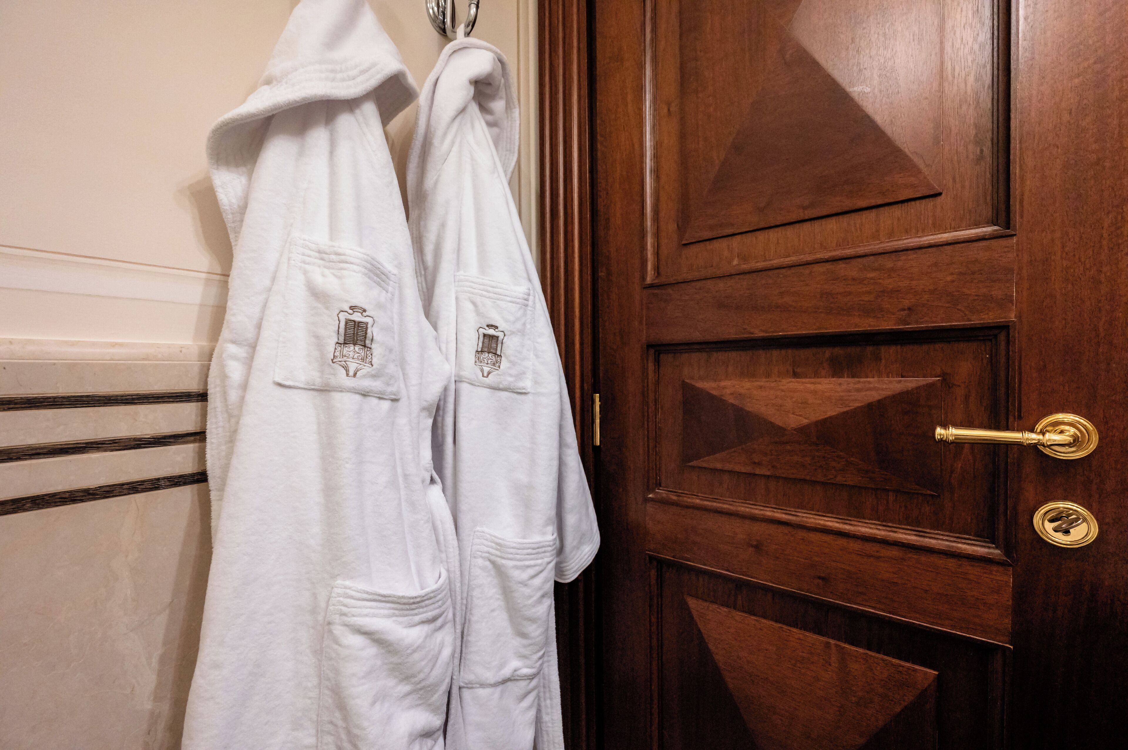 A wooden door with a brass handle and a towel rack with two white robes hanging on it.