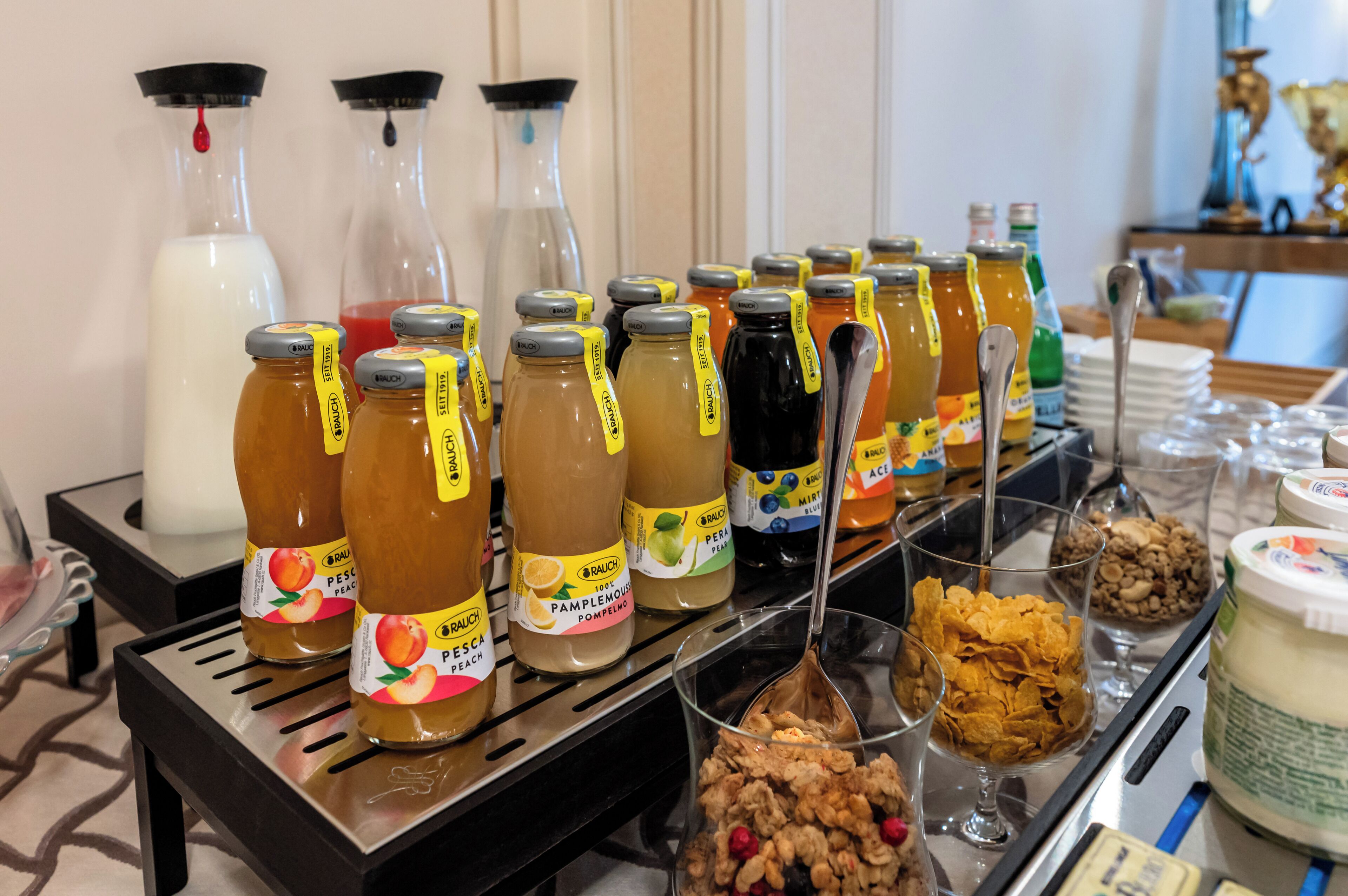 Ein reichhaltiges Buffet mit verschiedenen Speisen und Getränken, darunter Gläser mit Marmelade und eine Joghurt-Schale.
