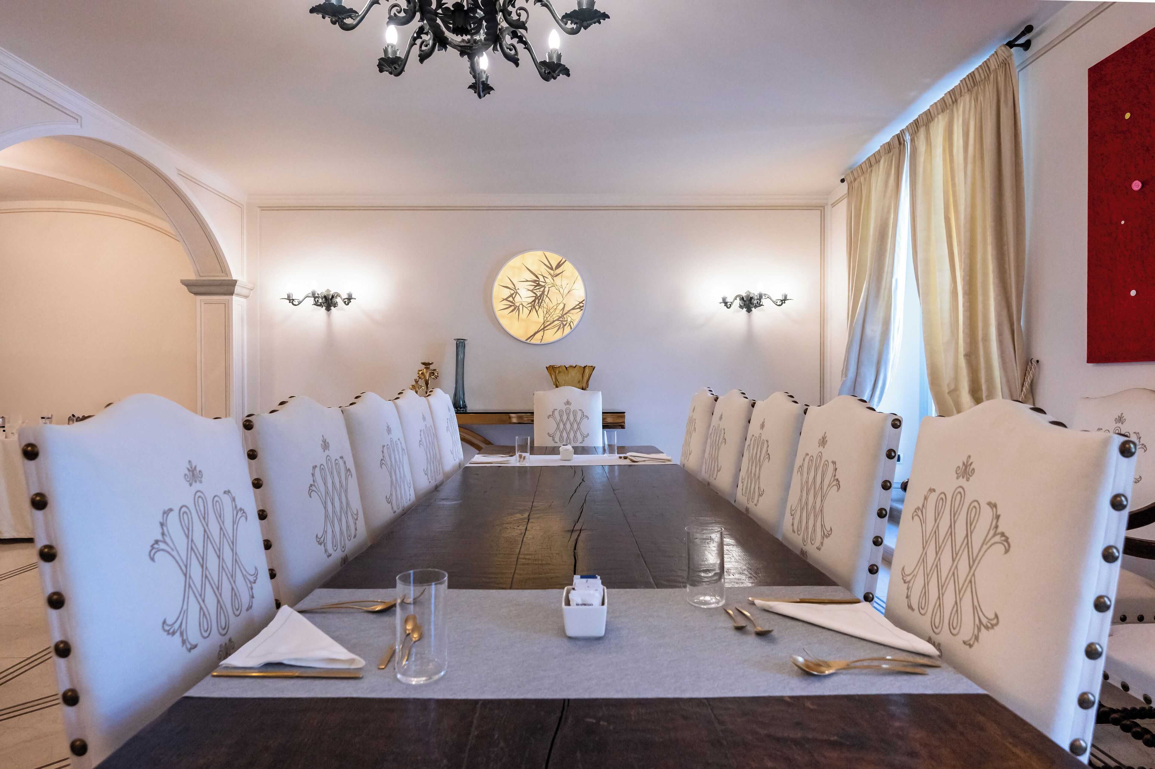 Une longue table à manger avec des chaises rembourrées, un lustre et des appliques murales.