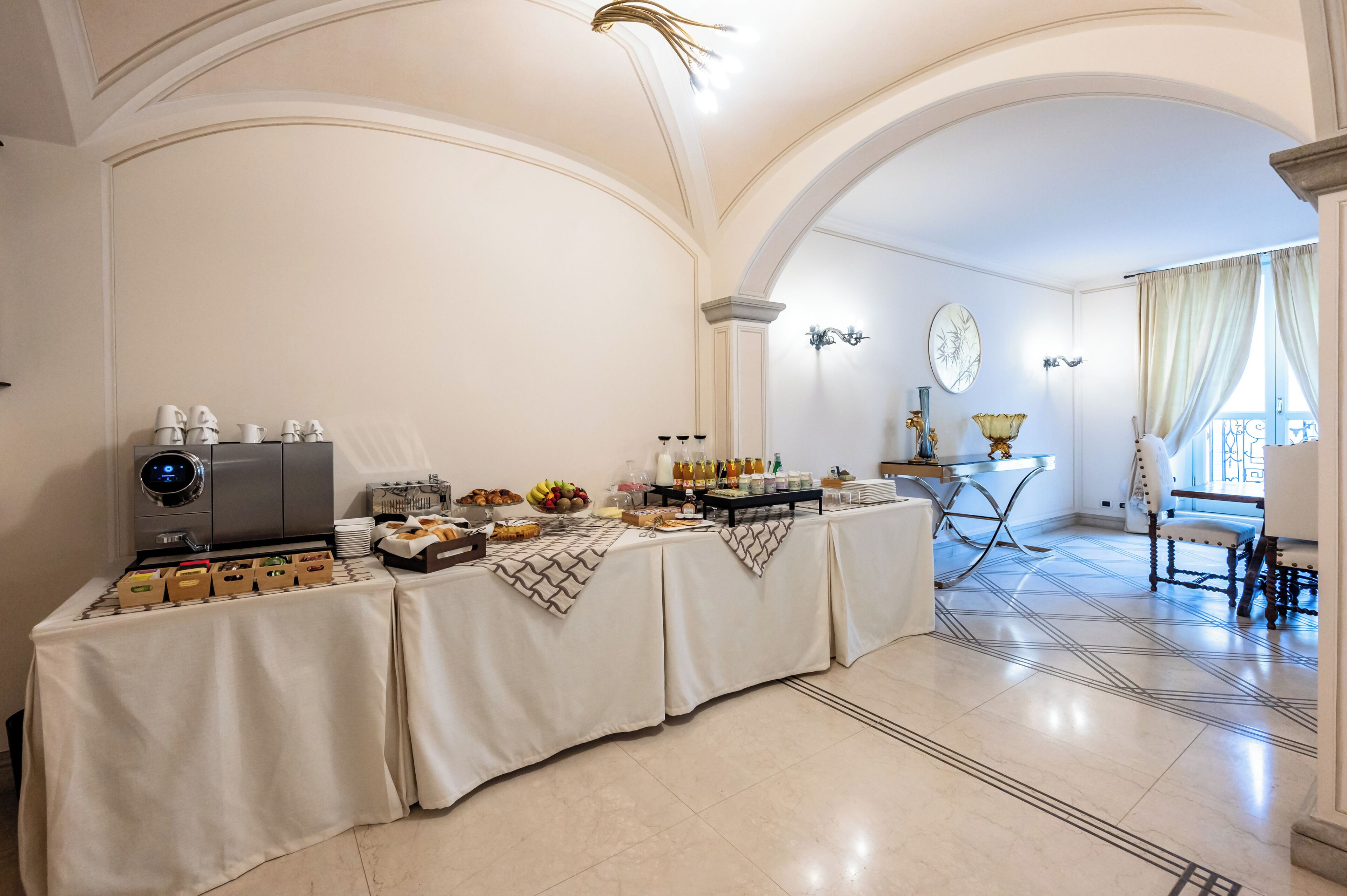 A breakfast buffet setup in a room with white walls and a high ceiling.