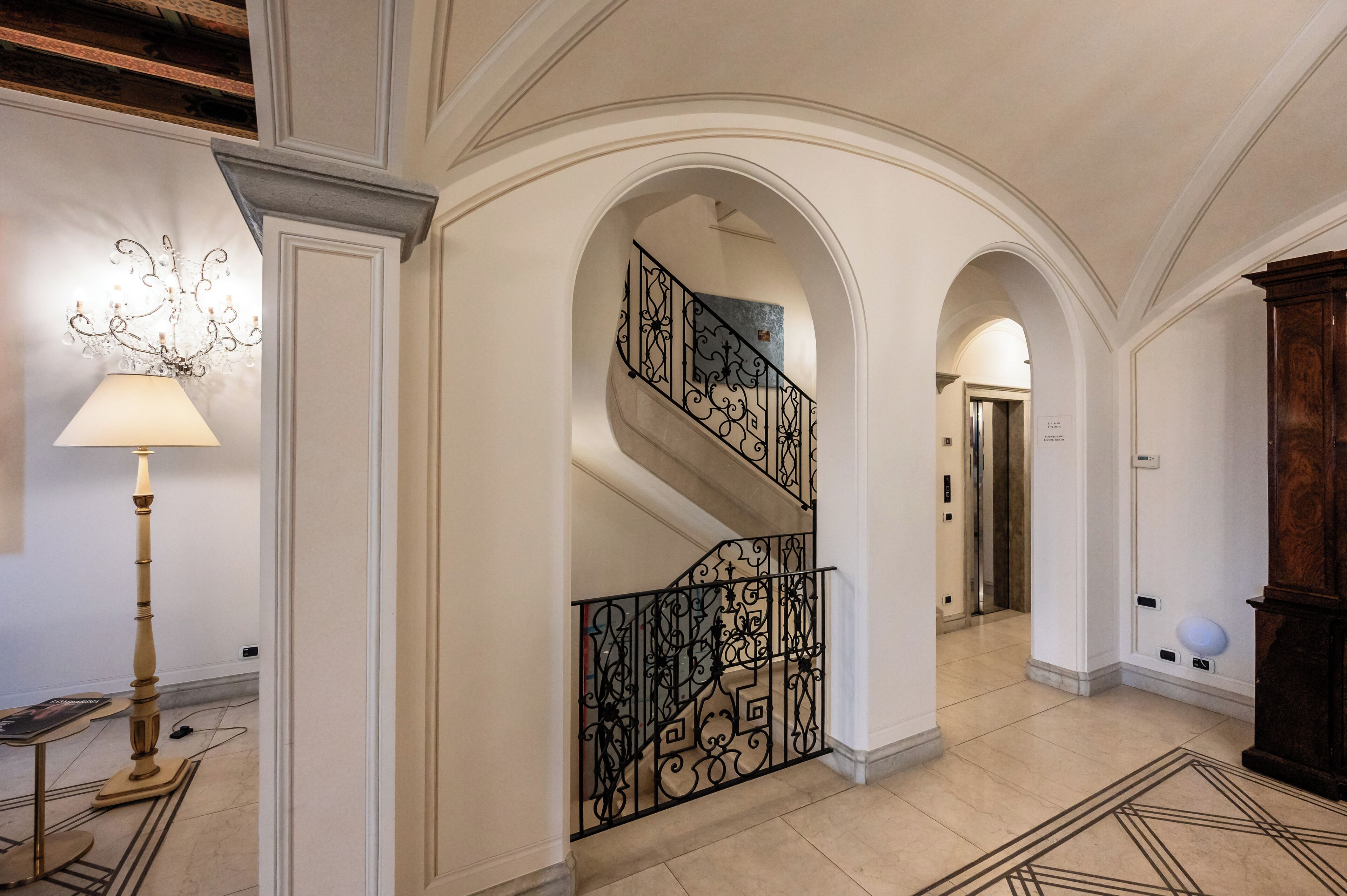 Eine prachtvolle Diele mit einer Treppe, die mit aufwändig gearbeiteten schwarzen Geländern, einem Kronleuchter und einem gemusterten Teppich ausgestattet ist.