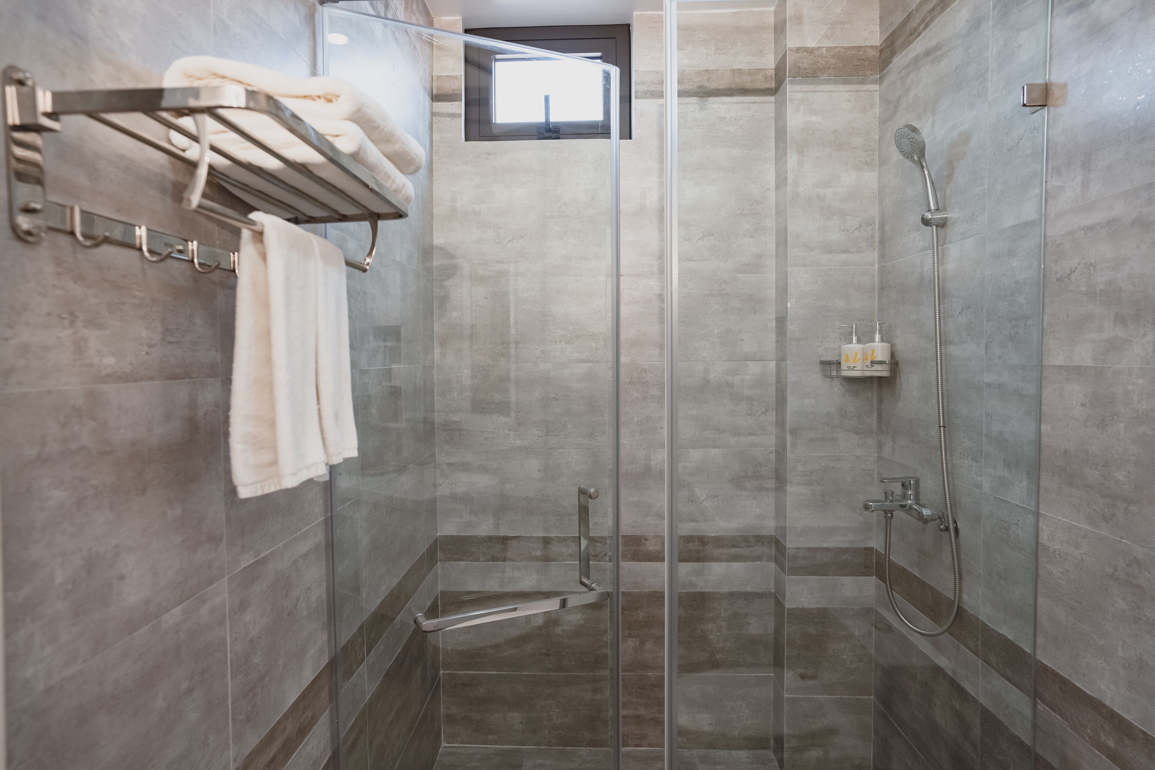 A modern shower area with a glass door, a towel rack with towels, and a showerhead.