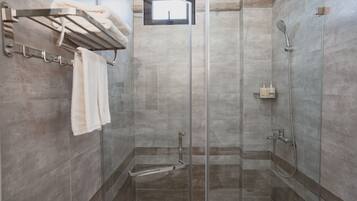 A modern shower area with a glass door, a towel rack with towels, and a showerhead.