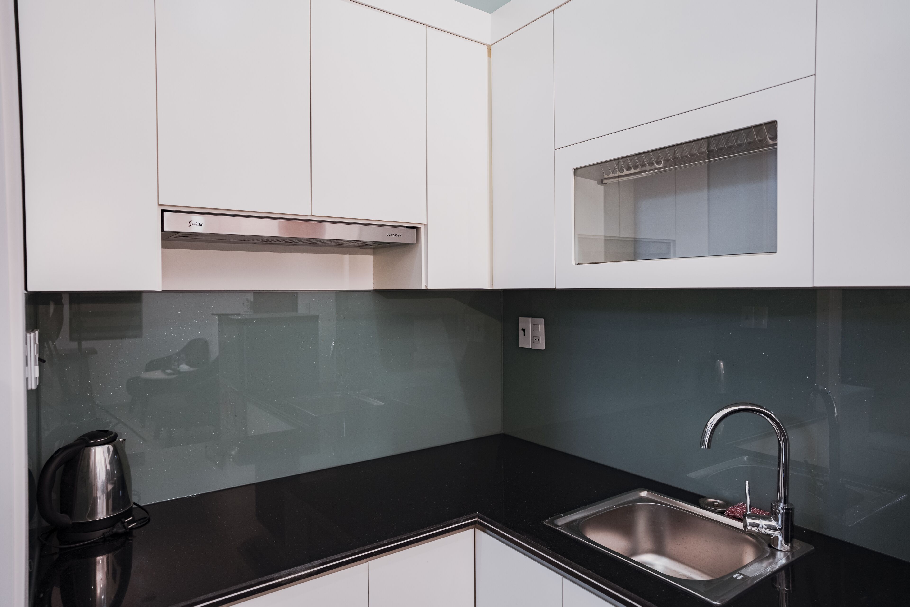 A modern kitchen with white cabinets, a black countertop, a stainless steel sink, and a built-in range hood.