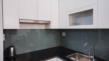 A modern kitchen with white cabinets, a black countertop, a stainless steel sink, and a built-in range hood.