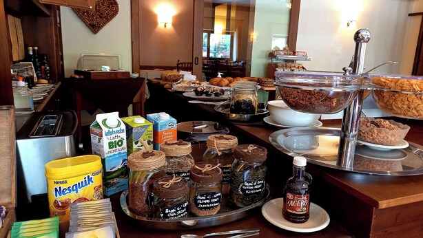 A breakfast buffet with various food items, including jars of spreads, a bottle of syrup, and cartons of milk. - Hotel Comelico (Padola)