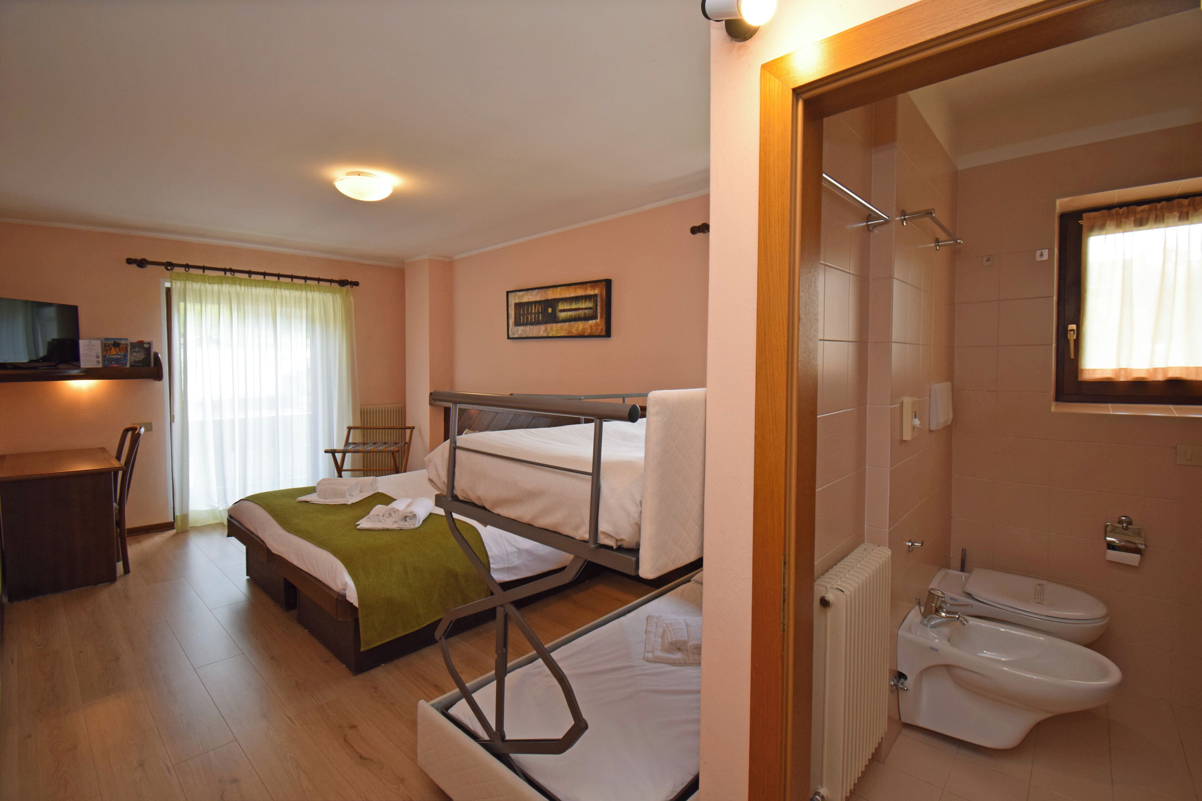 A hotel room with bunk beds, a desk, a chair, a shower, and a toilet.