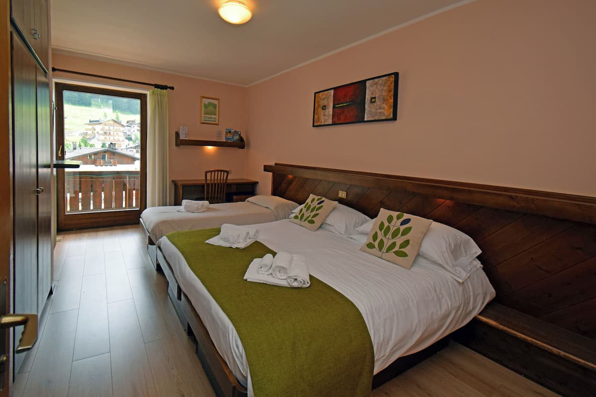 A hotel room with two beds, a balcony, a chair, and a small table.