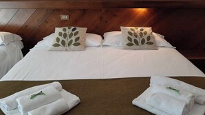A hotel room with a wooden ceiling, two beds with white linens, and decorative pillows with a leaf pattern. There are towels on the bed and a brown headboard. - Hotel Comelico (Padola)