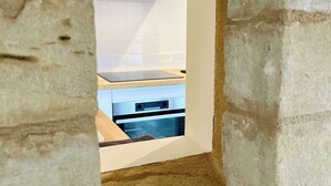 A stone-framed window opening to a modern kitchen with white tiles, a stove, and a hanging light fixture.