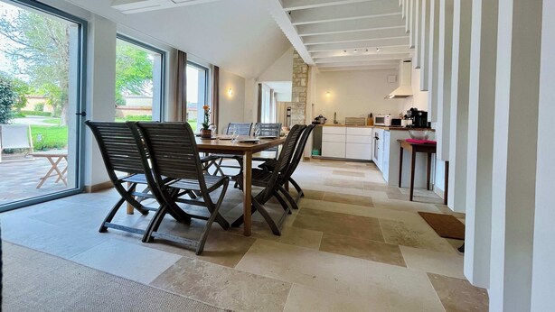 A modern kitchen with white cabinets, a dining area with a wooden table and chairs, and a staircase leading to an upper level.