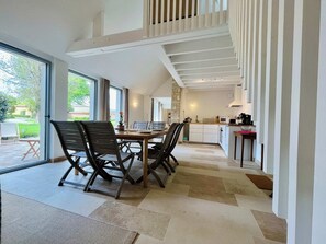 Una cocina moderna con armarios blancos, un comedor con mesa y sillas de madera, y una escalera que sube a un nivel superior.