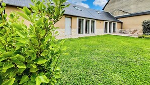 A modern house with a well-maintained lawn, a patio with outdoor furniture, and a large windowed room.