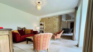 A living room with a red sofa, patterned armchairs, a wooden cabinet, and a stone wall.