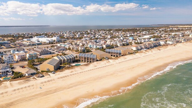 Luchtbeeld van een kustplaats met huizen en een hotel aan het strand, met uitzicht op het strand.
