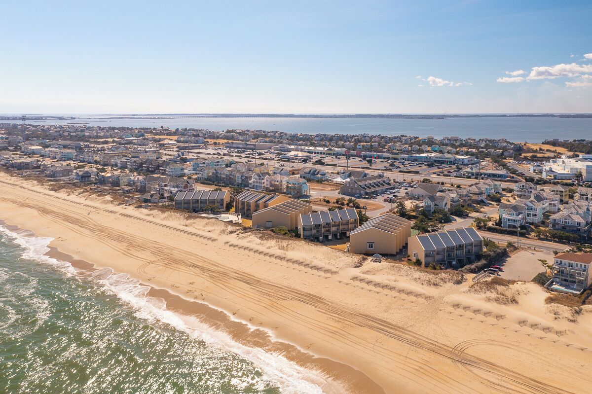 A coastal residential area with houses near the beach, featuring a mix of single and multi-story buildings, and a clear view of the ocean.