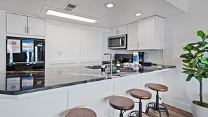 Una cocina moderna con armarios blancos, una isla grande con taburetes, un microondas y un refrigerador.