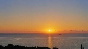 Solnedgang over et roligt hav med et fjernt skib og en silhuet af en kystlinje.