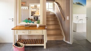 A staircase leading to a bathroom with a sand dune mural, a wooden console table with a mirror, and a wicker basket with a bottle. - Thatched roof vacation home Ankerplatz in Fuhlendorf am Bodden (Fuhlendorf)