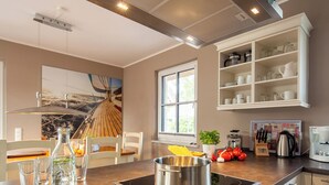 A modern kitchen with a central island, a built-in oven, and a window providing natural light. - Thatched roof vacation home Ankerplatz in Fuhlendorf am Bodden (Fuhlendorf)