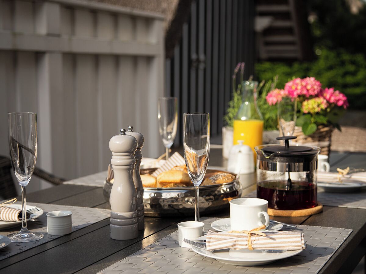Een gedekte tafel met een koffiepot, zout- en peperstel, een bord gebak en een kop koffie.