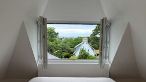 A bedroom with a large window, white walls, and a bed. - "La Pagode"close to beache (Trégastel)