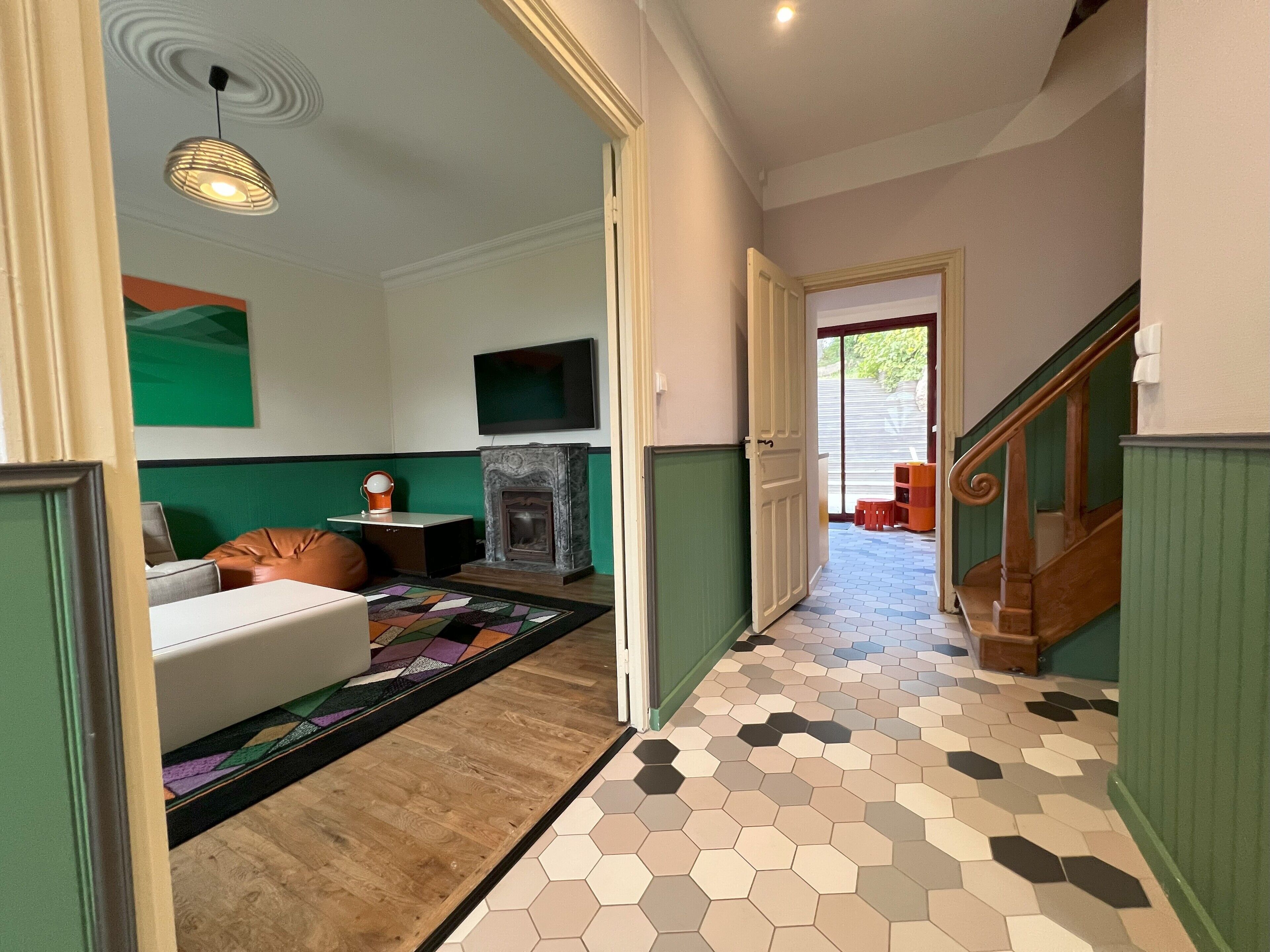 Un pasillo con piso de madera, pared verde, chimenea, televisor y escalera.