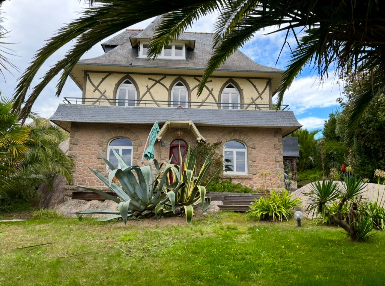 A two-story house with a stone facade, multiple windows, and a well-maintained garden with various plants.
