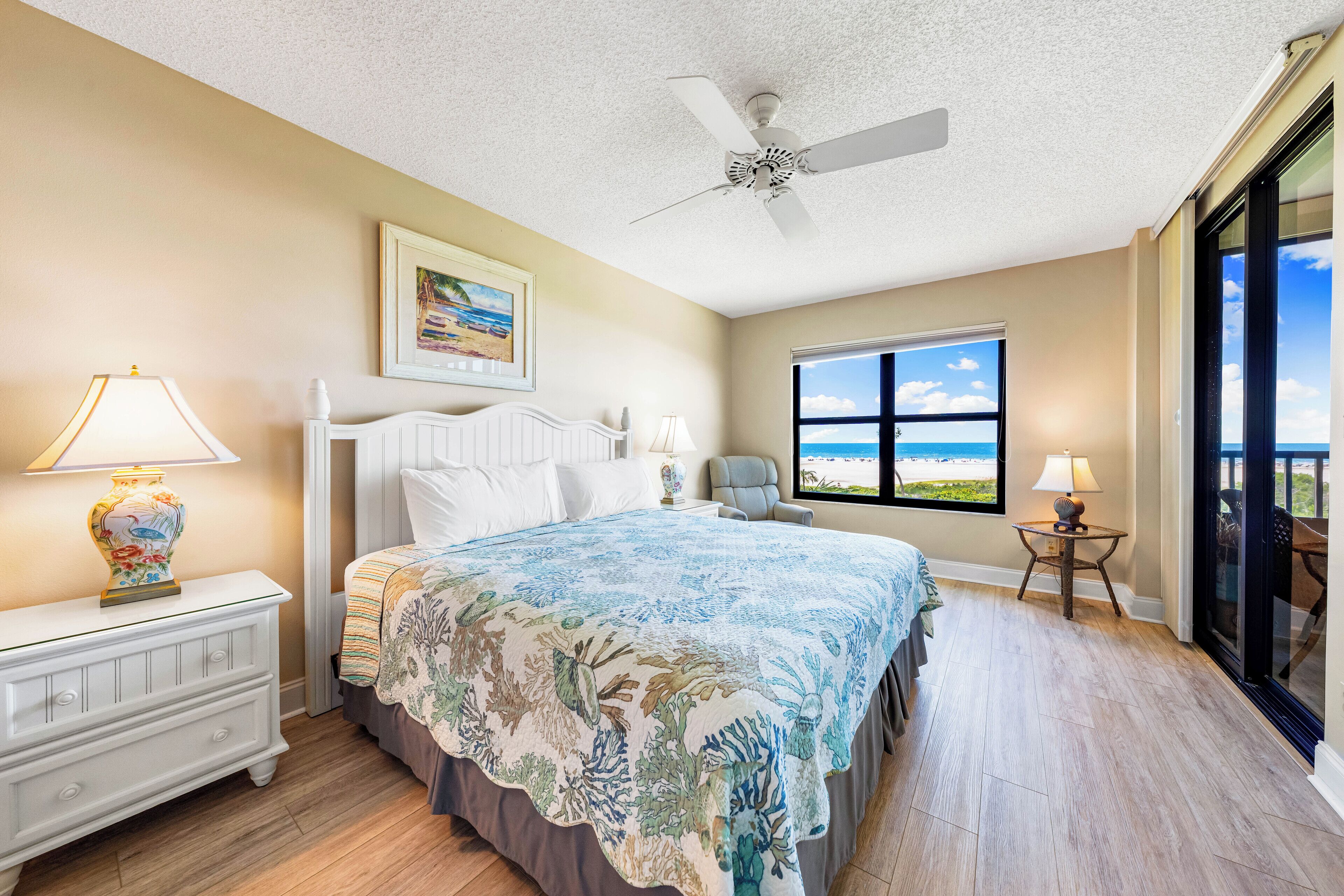 A bedroom with a bed, a nightstand, a chair, a window with a view, and a ceiling fan.