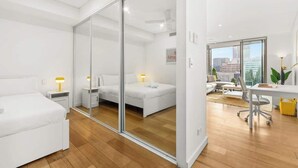 A modern hotel room with a large sliding glass door, a bed, a desk, and a view of the city.