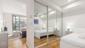A modern bedroom with a large bed, a desk, and a chair. There is a sliding glass door leading to a balcony. - Central art-deco 1bed with balcony & aircon (Surry Hills)