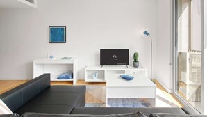 A modern living room with a sofa, a coffee table, a TV, and a plant. - Central art-deco 1bed with balcony & aircon (Surry Hills)