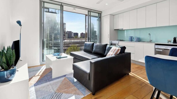 A modern apartment with a living area, kitchen, and large windows offering city views. - Central art-deco 1bed with balcony & aircon (Surry Hills)