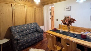 Um quarto acolhedor com paredes de madeira, um sofá azul estampado, uma mesa de jantar com cadeiras e um tapete branco e fofo.
