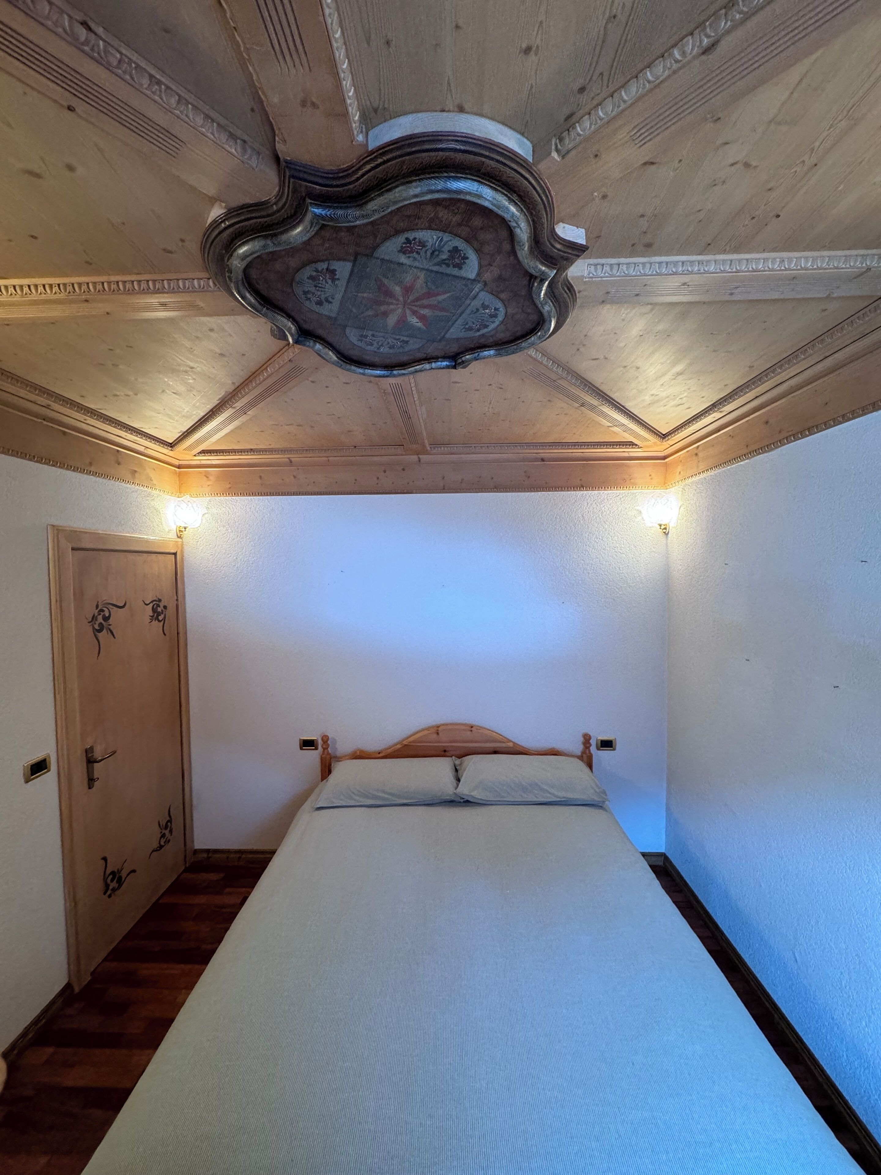 Een slaapkamer met een houten bed, een houten deur met decoratieve versieringen en een plafond met een decoratief ontwerp.