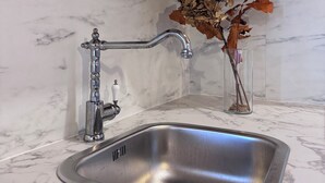 Cozinha com pia de aço inoxidável, bancada de mármore, armários de madeira e um vaso decorativo com folhas secas.