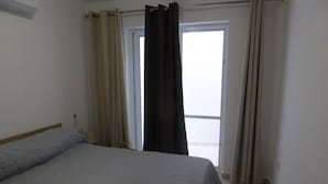 A bedroom with a bed, a window with curtains, and a door. - Seaview Ground Floor Flat Wheelchair Friendly (Zebbug)