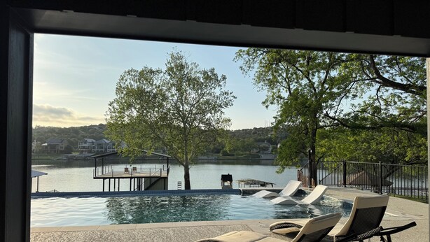 An outdoor swimming pool with lounge chairs and a dock extending into the water. - Luxury Lakefront Living in Marble Falls: Pool, Private Dock & Endless Views! (Marble Falls)