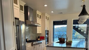 A modern kitchen with a stainless steel refrigerator, oven, and stove, wooden cabinets, and a large island with bar stools. - Luxury Lakefront Living in Marble Falls: Pool, Private Dock & Endless Views! (Marble Falls)