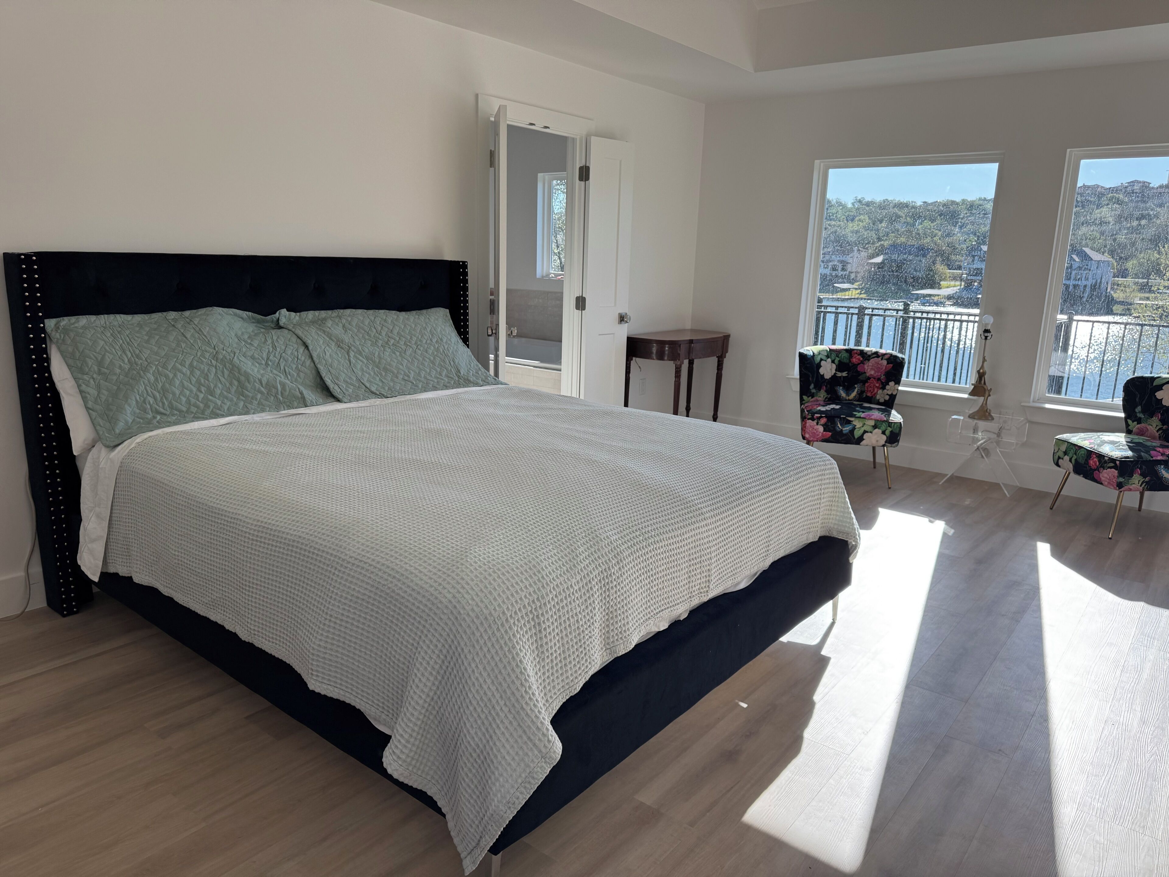 A bedroom with a large bed, a door leading to a balcony, and a view of a balcony with a railing.
