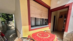 A patio area with a table and chairs, a window with blinds, and a stone staircase leading outside. - Apartment Marija 6 (Crikvenica)