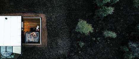 An aerial view of a cabin with a small deck area, surrounded by dense forest.