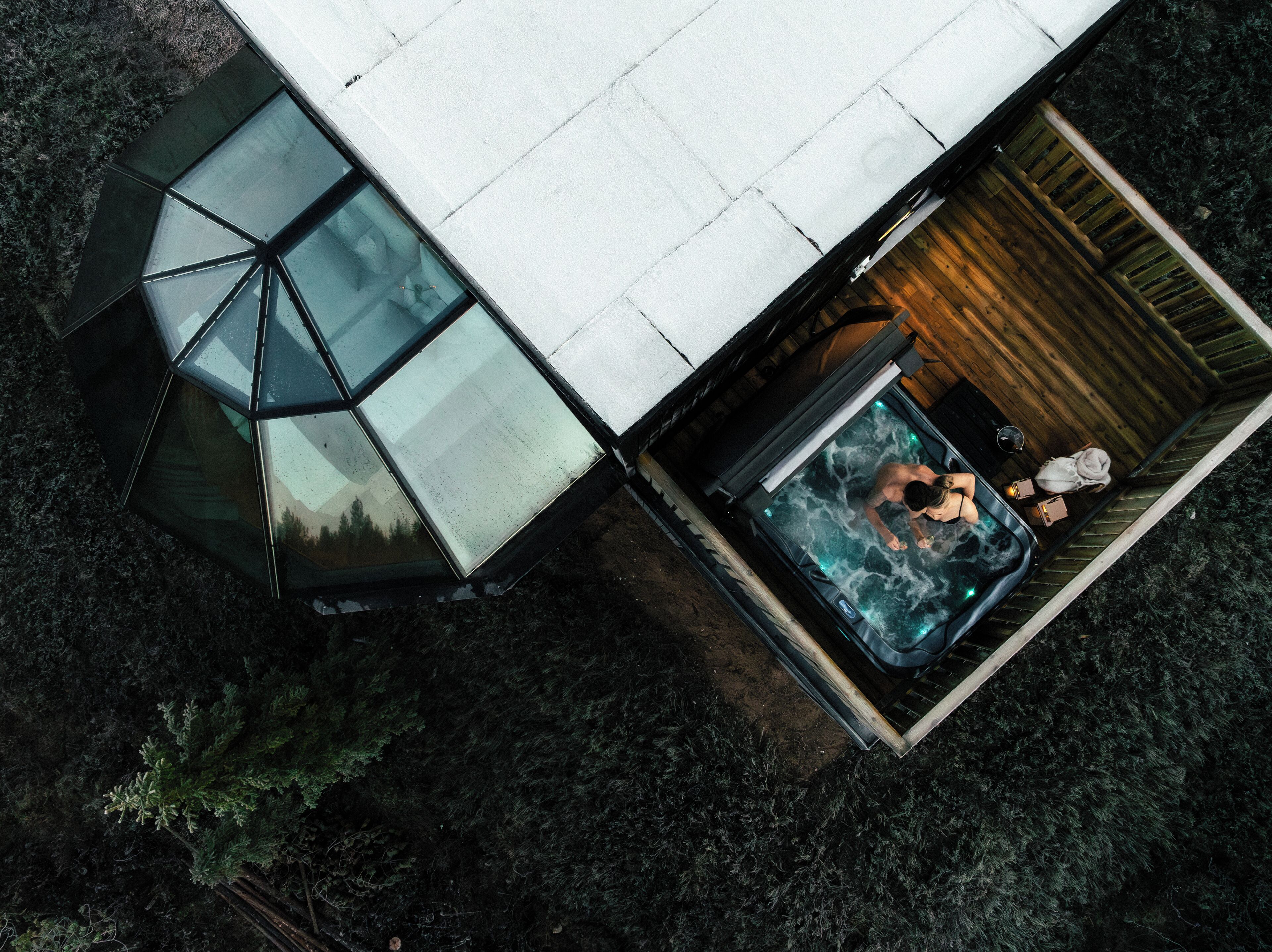 Una estructura moderna con techo de vidrio, jacuzzi y terraza de madera.