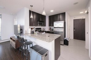 A modern kitchen with dark cabinets, stainless steel appliances, a granite countertop, and a bar area with stools.