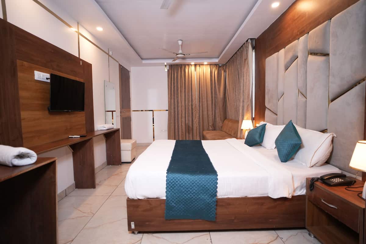 Une chambre d’hôtel dotée d’un grand lit, d’une tête de lit en bois, d’un téléviseur à écran plat fixé au mur, d’une table de chevet avec une lampe et d’un ventilateur de plafond.